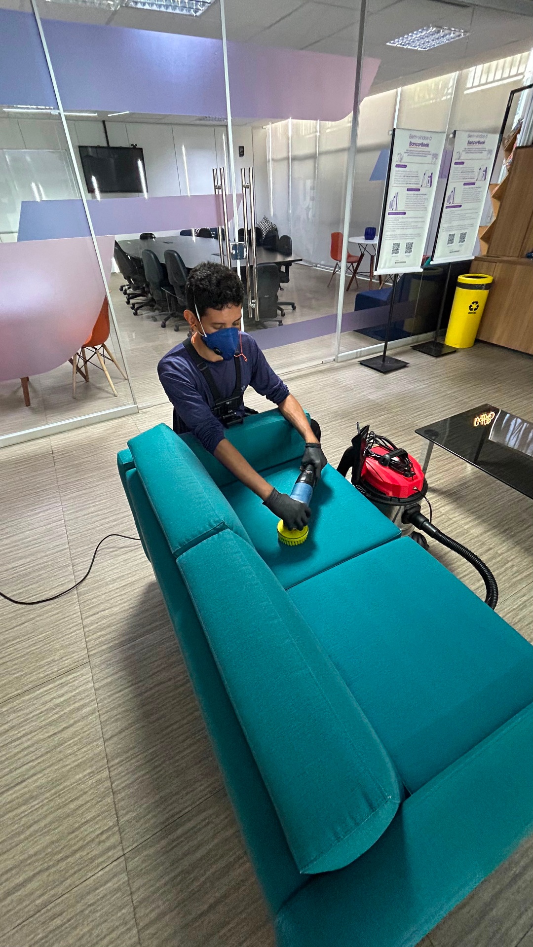 Técnico da Home Clean DF higienizando sofá corporativo teal em ambiente de escritório moderno